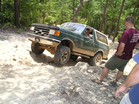 1996 Ford Bronco - A green Ford Bronco tackles a challenging off-road course on a sunny day.
