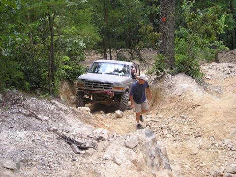 1996 Ford Bronco - A 1996 Ford Bronco tackles a challenging off-road path in a wooded area.