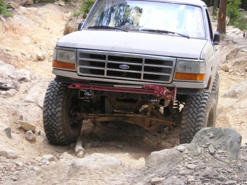 1996 Ford Bronco - A white Ford truck with off-road modifications tackles a challenging rocky terrain.