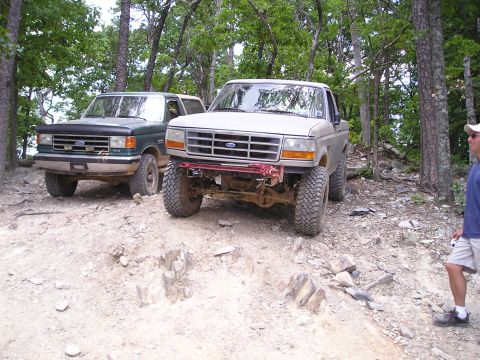 1996 Ford Bronco - Two Ford Broncos navigate a rocky, wooded trail, their off-road capabilities.