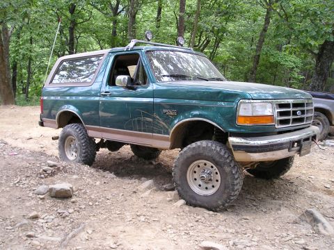 1996 Ford Bronco - A green 1996 Ford Bronco navigates a challenging off-road course with large tires and a lifted suspension.