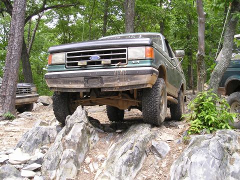 1996 Ford Bronco - A green Ford Bronco navigates a challenging rocky trail, with another vehicle visible in the background.