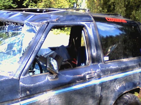 1987 Ford Bronco II - This 1987 Ford Bronco II shows significant damage to its windshield and roof, with visible rust and peeling paint.