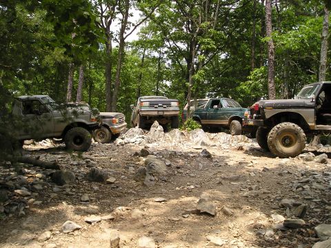 1996 Ford Bronco - Off-road vehicles tackle a challenging rocky path in a wooded area.