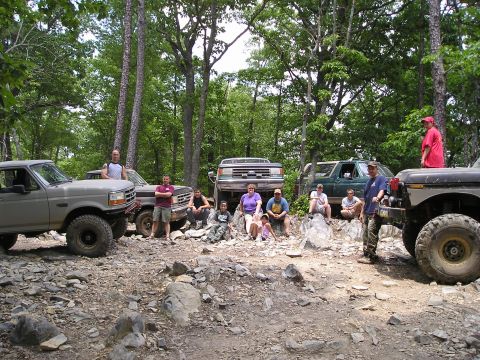 1996 Ford Bronco - Off-road enthusiasts and their vehicles gather on a rocky trail in a wooded area.