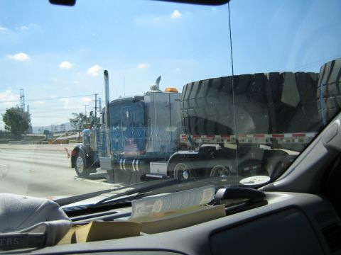 1990 Ford Bronco - semi truck carrying enormous earthmover tires is seen ahead through a windshield, with papers cluttering the dashboard.