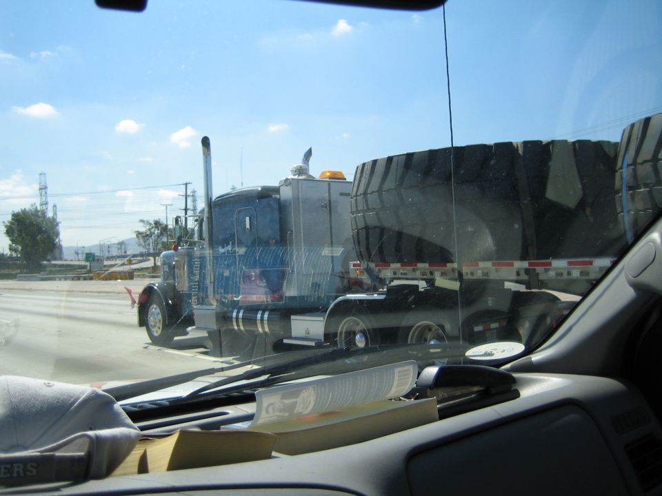 Semi truck hauling enormous earthmover tires seen through a windshield in traffic