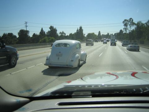 1990 Ford Bronco - silver vintage hot rod coupe drives ahead on a multi-lane highway, viewed over the dashboard of a following vehicle.