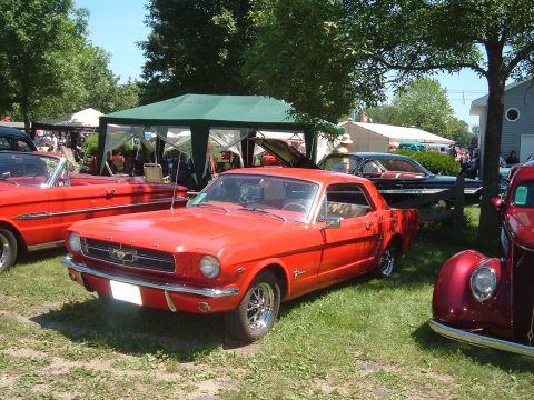 1994 Ford Bronco - A red 1965 Ford Mustang coupe is displayed at an outdoor event with other classic cars.