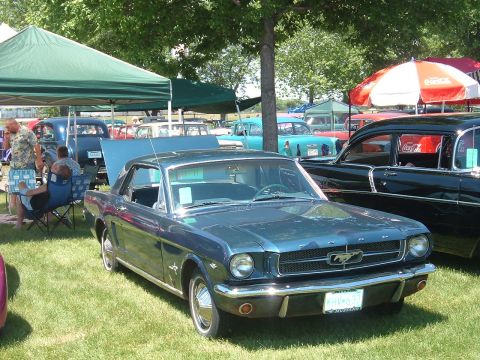 1994 Ford Bronco - A dark blue 1965 Ford Mustang coupe is parked on grass at an outdoor car show.