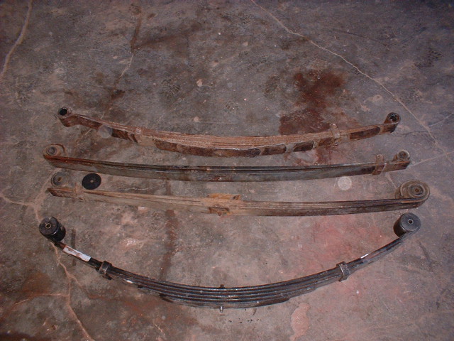Four leaf springs, one new and three rusty, laid out on a concrete floor