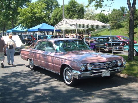 1994 Ford Bronco - A pink sedan is parked at an outdoor car show with other vehicles in the background.