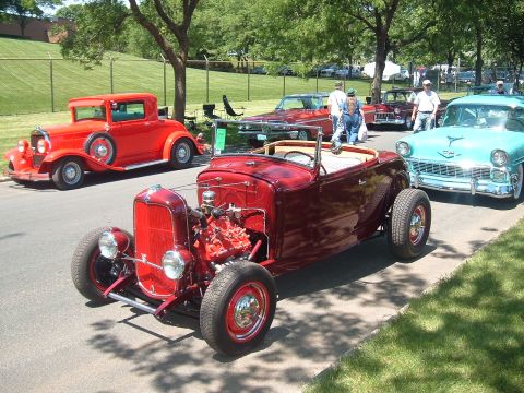 1994 Ford Bronco - A line of classic cars, including a red hot rod convertible and a turquoise 1950s sedan, are parked on a sunny day.