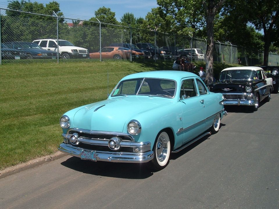 Light blue 1950 Ford sedan with whitewall tires parked on a street, other classic cars behind it