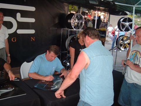 1994 Ford Bronco - Autograph session taking place at an event with custom car wheels on display in the background.
