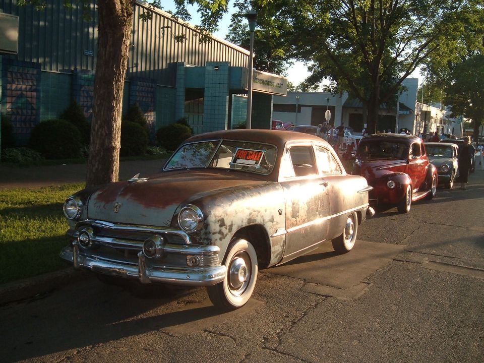 Rusty 1950 Ford Custom sedan with a "For Sale" sign in the windshield, parked on a street