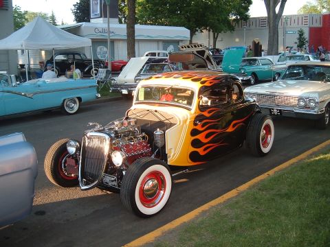 1994 Ford Bronco - A custom hot rod with a flame paint job is displayed at a car show with other vehicles.