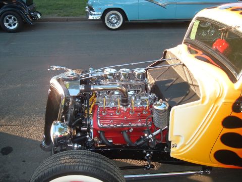 1994 Ford Bronco - A detailed view of a hot rod's engine compartment, with another classic car parked nearby.