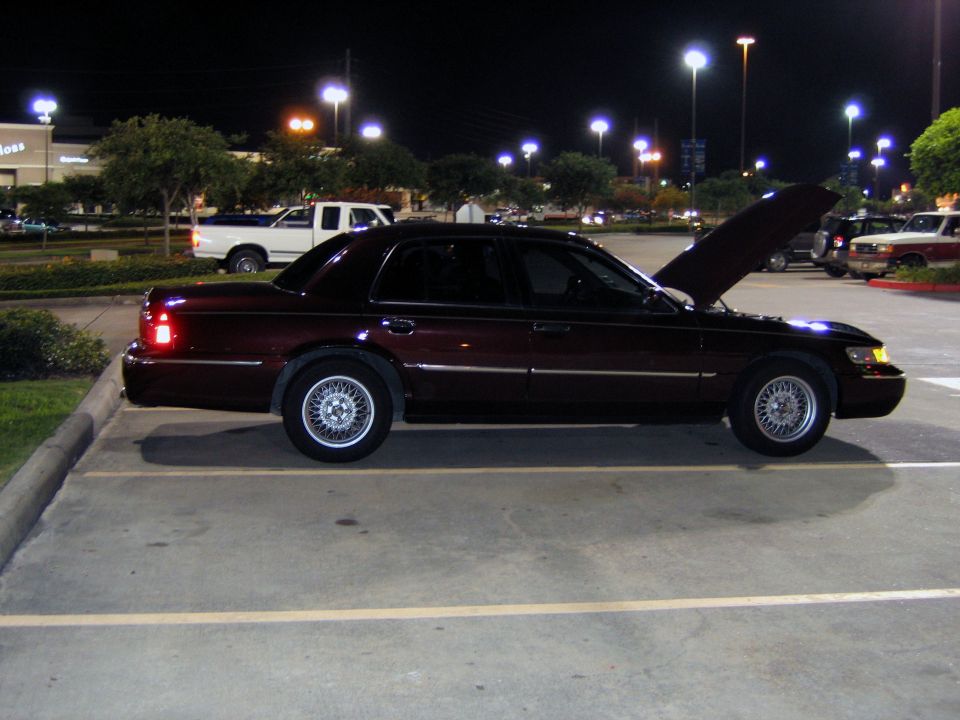 Dark maroon Mercury Grand Marquis sedan in side profile at night with hood up and wire wheels