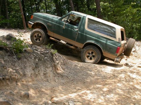 1990 Ford Bronco - A green Ford Bronco navigates a steep dirt trail with a flat front tire.