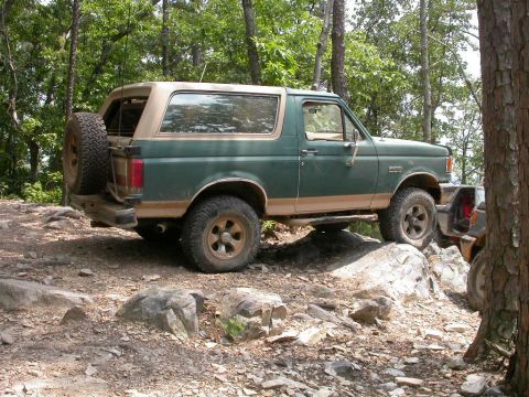 1990 Ford Bronco - 1990 Ford Bronco navigating a rocky trail in a wooded area.