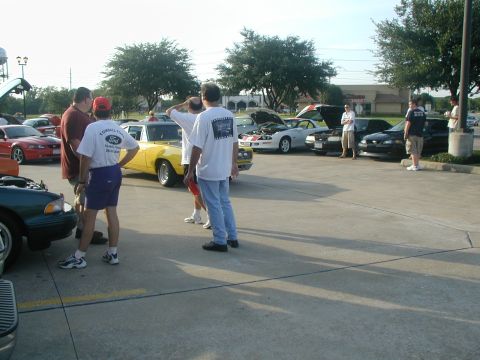 2000 Ford Crown Victoria - A group of people gather around various cars parked in an outdoor lot.