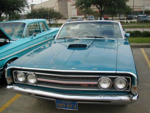 2000 Ford Crown Victoria - A teal 1968 Ford Torino GT convertible is parked next to another classic car, its distinctive hood scoop and front grille.