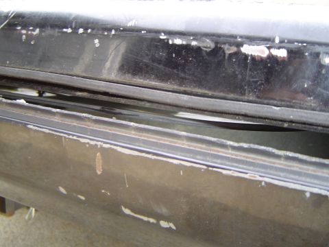1989 Ford Bronco - Close-up of a worn black tailgate window seal, showing damage and exposed metal.