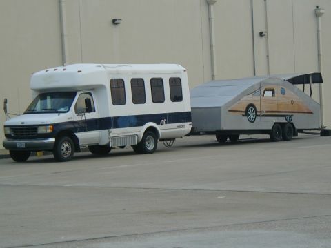 2000 Ford Crown Victoria - A white Ford E-Series bus tows a custom-built trailer with a unique graphic design.