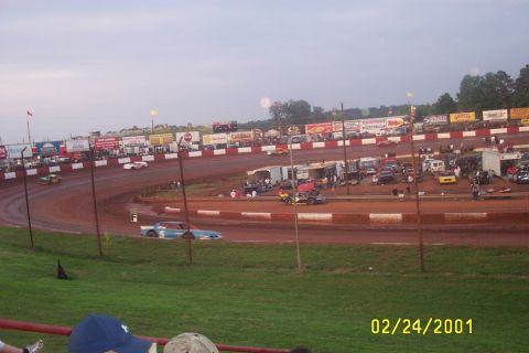 1979 Ford F-150 - A dirt racetrack with multiple cars racing and spectators in the stands.