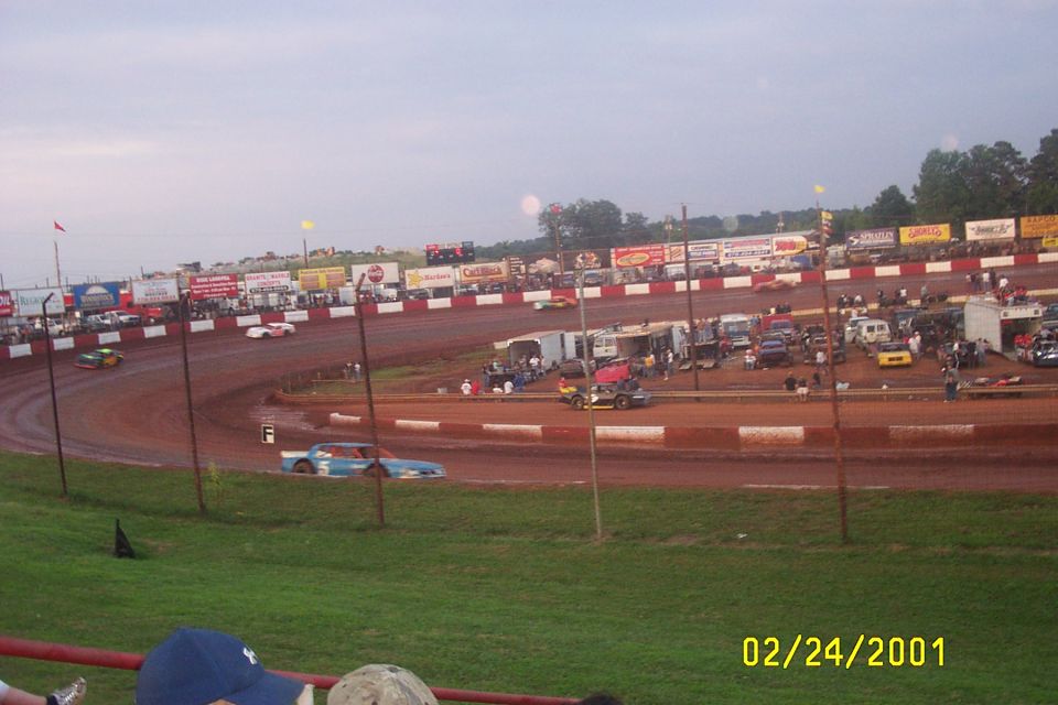 Dirt racetrack with several race cars on the track and parked in the background