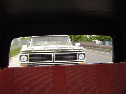 1972 Ford F-100 - View of a white 1972 Ford F-100 truck from inside another vehicle, showing its distinctive front grille.