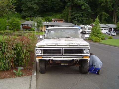 1972 Ford F-100 - A person works on the front tire of a white Ford F-series truck parked on a residential street.
