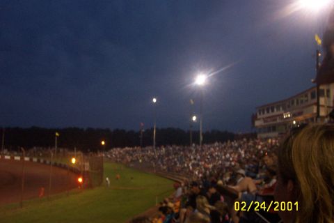 1979 Ford F-150 - A large crowd gathers at a race track under a dark sky, illuminated by stadium lights.