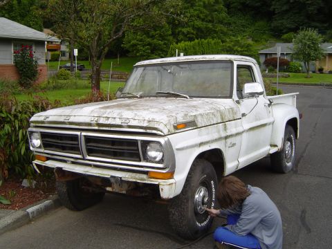 1972 Ford F-100 - Person checks the tire on a weathered white Ford F-Series truck from the early 1970s.