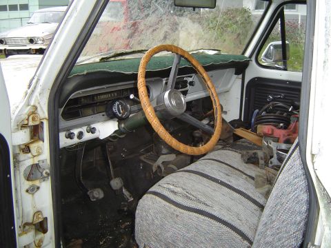 1972 Ford F-100 - The interior of a vintage pickup truck shows a worn steering wheel, dashboard, and a striped seat cover.
