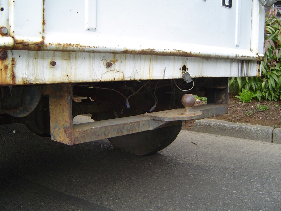 Rear of a white truck with a rusty bumper and a trailer hitch with a ball mount