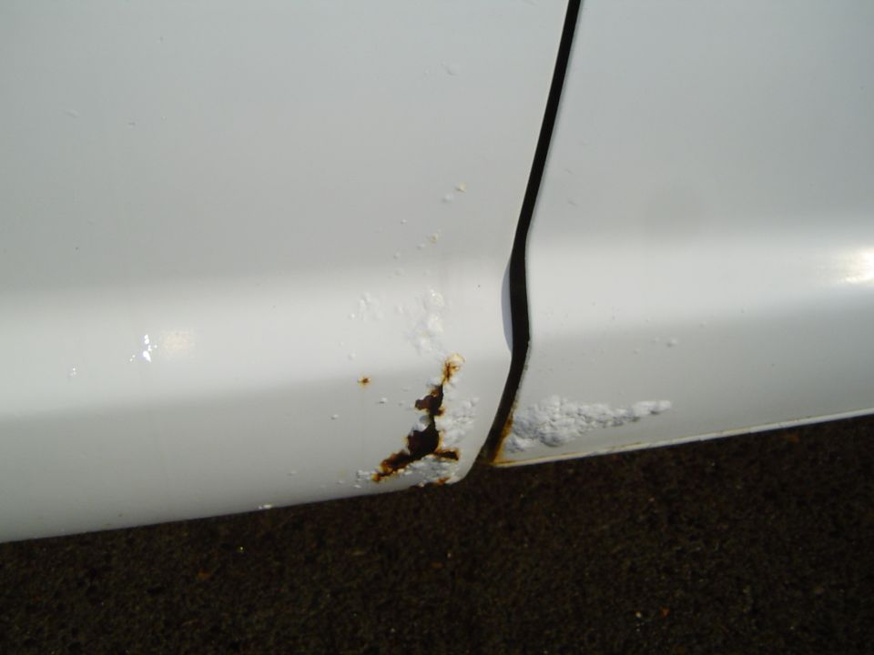 White truck door seam showing significant rust and bubbling paint along the bottom edge