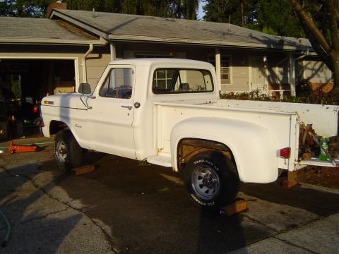 1972 Ford F-100 - A white pickup truck is parked on a driveway in front of a house, supported by wooden blocks.