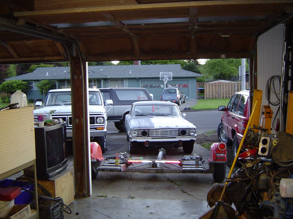 Primered mid-1960s sedan on a frame stand in a driveway seen from inside an open garage