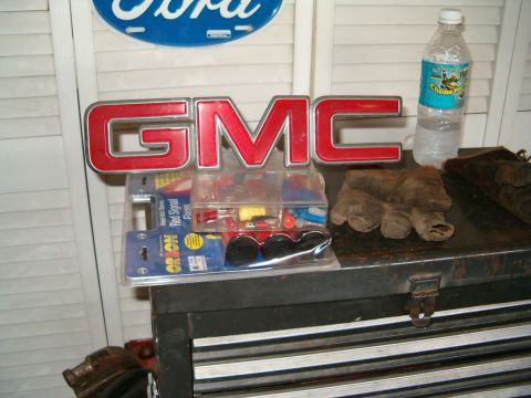 1991 Ford Bronco - A collection of automotive parts and a GMC emblem are displayed on a toolbox, with a Ford sign above.