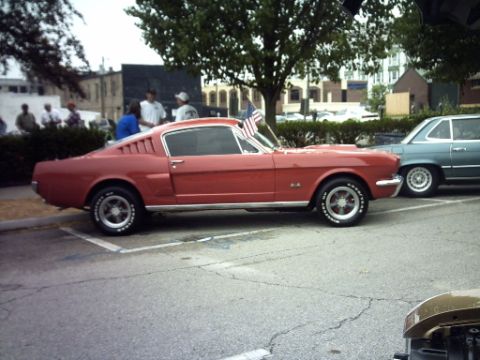 1995 Ford Probe - A red 1965 Ford Mustang fastback is parked next to another vehicle, adorned with American flags.