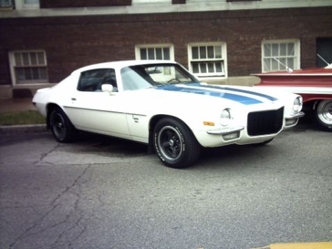 1995 Ford Probe - A white 1970s Chevrolet Camaro with blue racing stripes is parked next to a red car.