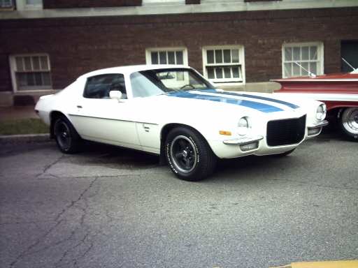 White 1970s Chevrolet Camaro with blue racing stripes parked next to a red car