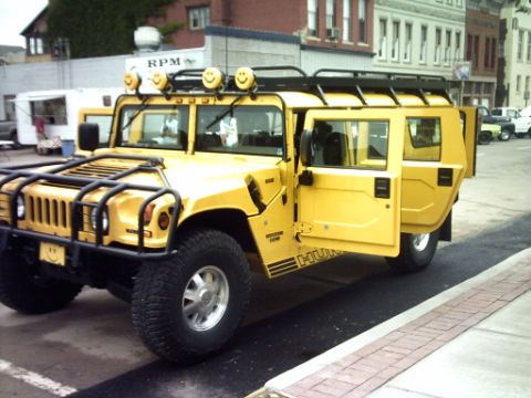 1995 Ford Probe - A bright yellow Hummer H1 is parked with its doors open, smiley face lights on the roof.