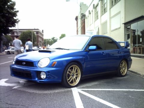 1995 Ford Probe - A blue Subaru Impreza WRX with gold wheels is parked on a city street.