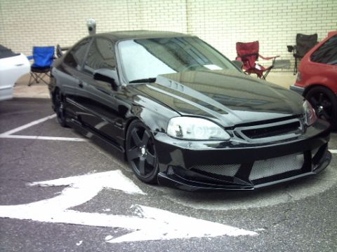 1995 Ford Probe - A modified black coupe is parked in a lot, with other vehicles and chairs visible in the background.