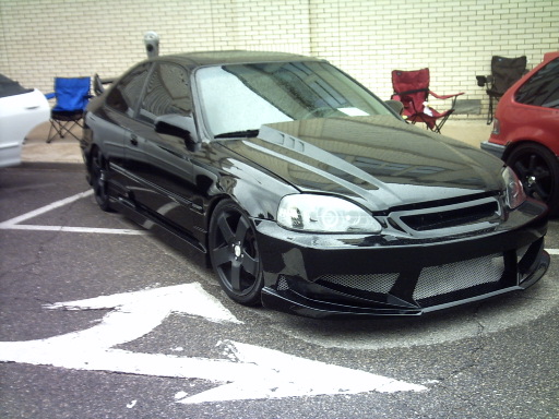 Black coupe with aftermarket body kit and hood scoop, parked in a lot