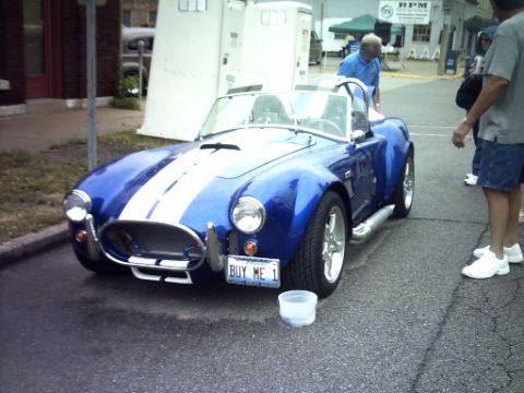 1995 Ford Probe - A blue convertible sports car with white racing stripes is parked on a street, with people standing nearby.