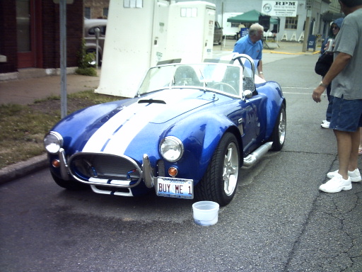 Blue convertible sports car with white stripes. License plate says BUY ME 1